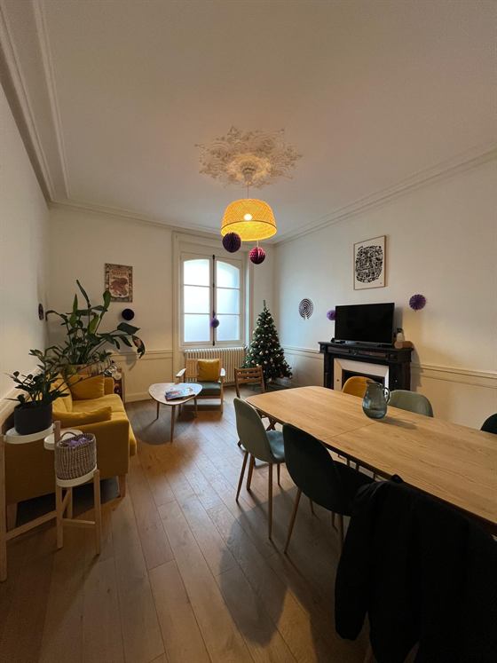 Salon commun avec canapé jaune, grande table en bois et cheminée